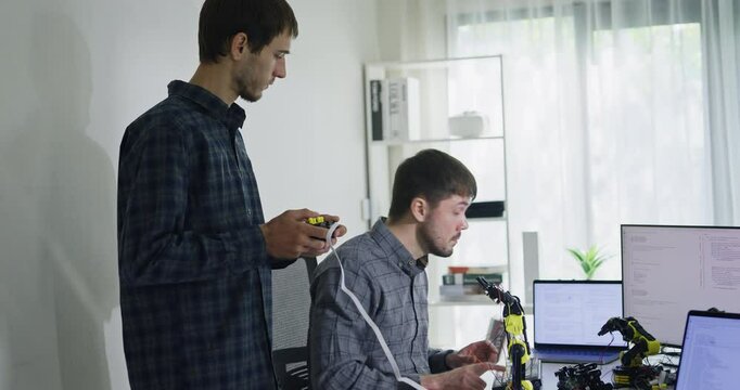 Team adult male engineer collaborate on robotic hand project using AI code solutions machine learning at tech workspace. Artificial intelligence interface, collaboration support prototype development.