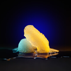 Ice melting. Melting ice chunks on dark background. Colored blue yellow backlight. Selective focus