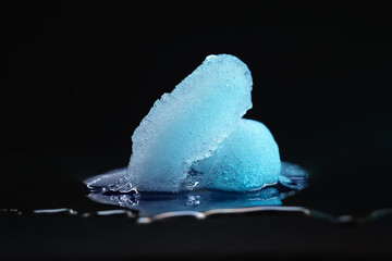 Ice melting. Pieces of melting ice on a dark background. Blue backlight. Selective focus