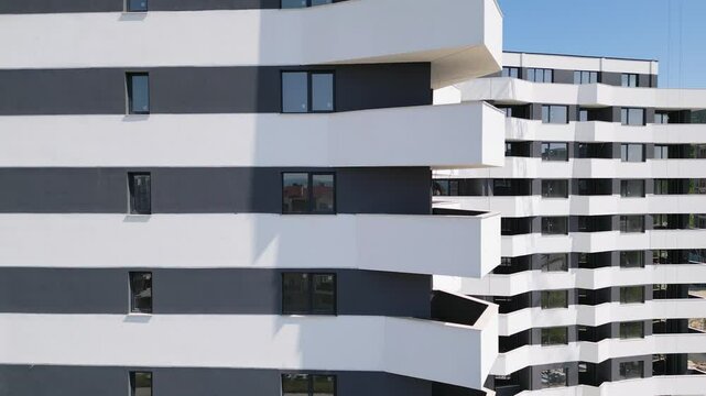Drone flyby along the facade of a modern residential building with white and dark gray accents, showcasing geometric balconies and large windows