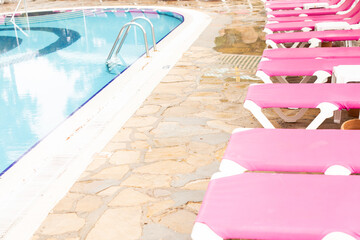 A row of pink deck chairs standing near hotel swimming pool.