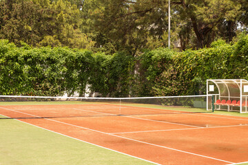 Empty tennis clay court surrounded by green hedge in a sunny day