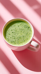 Fresh green matcha latte in a white cup on a pink background with light shadows.