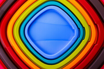 Overhead view of stacked plastic trays in vibrant rainbow colors forming a geometric pattern.