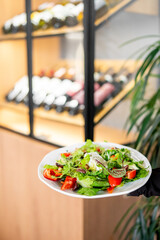 A vibrant salad with fresh vegetables and greens on a white plate, set in a restaurant with a wine rack in the background. Perfect for healthy dining and gourmet presentation.