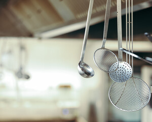 Stainless steel kitchen utensils hanging in a professional kitchen. Focus on ladles and skimmers...