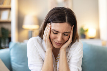 Woman, sick or headache pain in home for temple massage on sofa with frustrated face or loan...