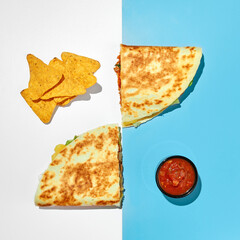 Two halves of quesadilla with chicken, cheese, vegetables, herbs and salsa sauce and nachos corn...