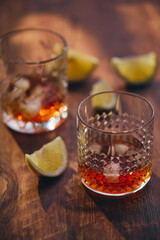 Glasses of whiskey with ice and lemon slices on a wooden table in the rays of light. Shallow depth of field