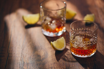 Glasses of whiskey with ice and lemon slices on a wooden table in the rays of light. Shallow depth of field