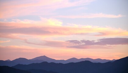 Obraz premium Dreamy cotton-candy sky with pearlescent clouds above a blurred silhouette of soft mountains at dusk