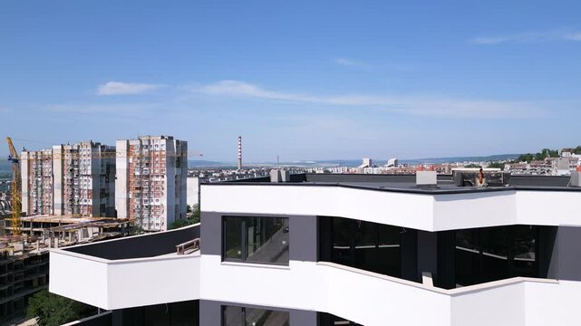 Drone flyby along the facade of a modern residential building with white and dark gray accents, showcasing geometric balconies and large windows