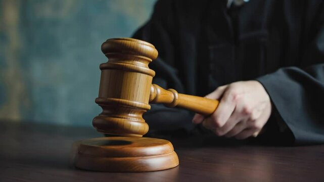 Judge's Hand Holding a Wooden Gavel Over a Sound Block, Symbolizing Justice and Verdict in a Courtroom