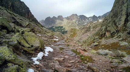 Obraz premium Rocky trail through the high Dolomites, framed by jagged mountain ranges and patches of snow, no humans
