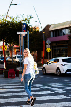 young adult Australian woman walking away down street over zebra crossing in urban area of town