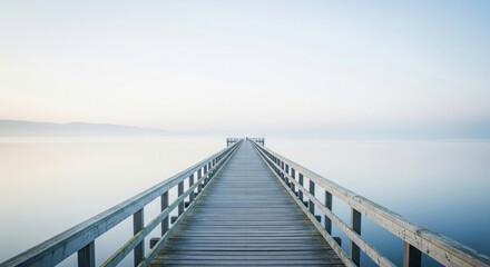 Naklejka premium A weathered wooden pier stretches into a soft mist over calm waters, blending sky and sea in a serene, endless horizon at dawn or dusk.