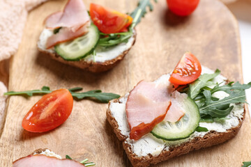 Wooden board of delicious sandwiches with cream cheese, ham and vegetables, closeup