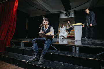Fototapeta premium A group of young actors engaged in a thoughtful performance on a stage with dramatic lighting and props. The scene portrays teamwork and creativity in a theater setting.