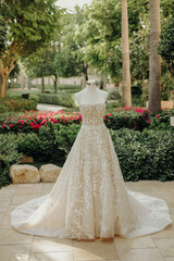 Close-up of white wedding gown with lace details. Artistic photo of wedding dress in green garden...