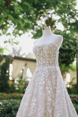 Close-up of white wedding gown with lace details. Artistic photo of wedding dress in green garden...