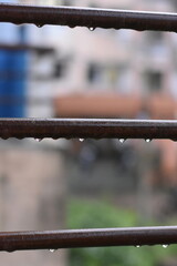 Raindrops clinging to horizontal bars of a railing, blurred city background.