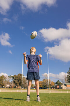 Junior rugby union player standing on field handling ball with goal posts in background
