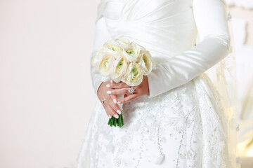 Elegant bride in a white wedding dress holding a bouquet of white roses. Close-up of hands and...
