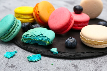 Board with sweet macaroons and blueberries on grey background