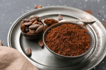 Bowls with cocoa powder and beans on black background