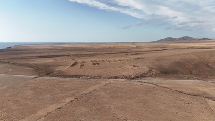 Desert landscape with dry vegetation, mountains in the background, and a wide sky