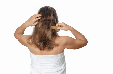 Back view of woman with bare shoulders combing her medium hair with wooden comb on white...