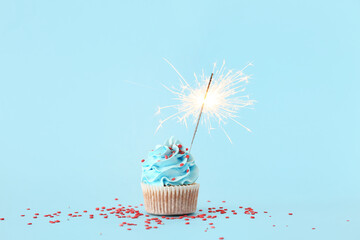Tasty birthday cupcake with sparkler on blue background