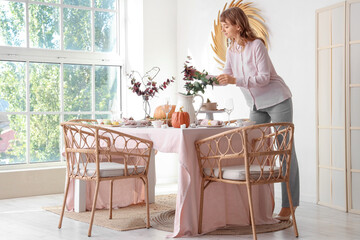 Beautiful young woman decorating table for Thanksgiving Day dinner in dining room