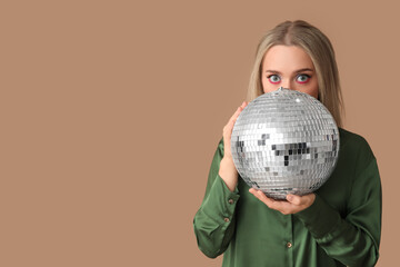 Beautiful young woman with disco ball on brown background