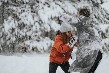 A playful scene of two individuals having a snow fight in a snow-covered forest during winter,...