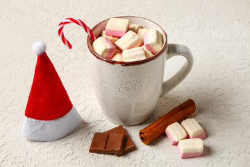 Cup of hot chocolate with marshmallows, candy cane and Santa hat on white table
