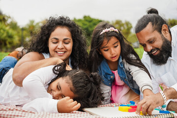 Naklejka na ściany i meble Happy indian family having fun playing with children outdoor at city park - Summer time and parenthood concept - Main focus on female kid face