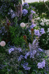 Lush garden floral arrangement with violet and white flowers, captured in natural sunlight. A...