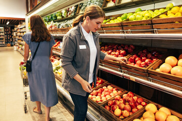 Female grocery store worker stands by the shelves as buyer with a cart walks past