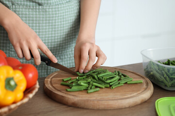 Woman cutting green beans for freezing on wooden table in kitchen, closeup