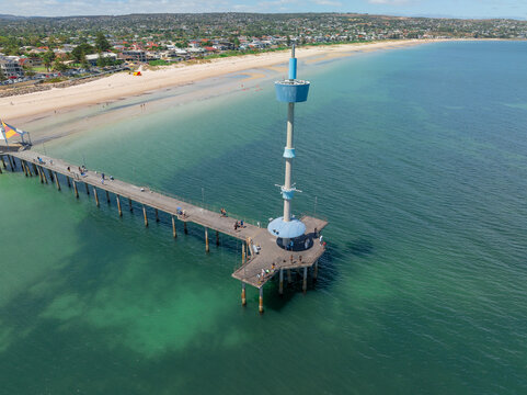 Fototapeta Aerial view of a beacon tower on the end of a coastal pier over a calm ocean turquoise ocean