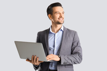 Handsome businessman using laptop on light background