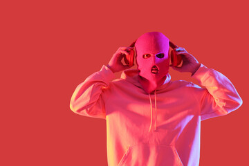 Handsome young man in balaclava with headphones on red background
