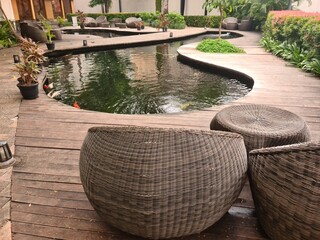 A koi fish pond in a public area with nearby empty rattan chairs, offering a peaceful and quiet moment in a commercial environment.