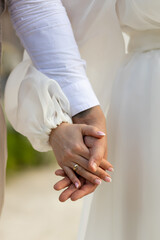 Newlyweds holding hands. Bride in white dress holding groom's hand in white shirt. Tender photo of...
