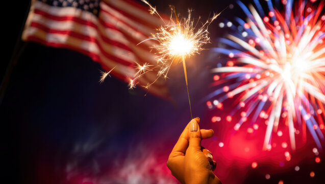 Hand holding sparkler celebrating with fireworks and american flag