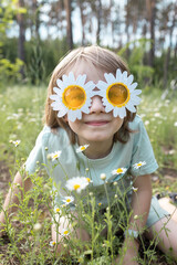 child sitting among blooming daisies in funny glasses in shape of flowers on sunny day. be positive, summer mood, pampering. happy carefree childhood. portrait of cute boy walking in park in summer