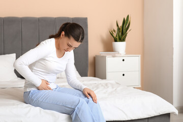 Young woman suffering from cystitis on bed at home