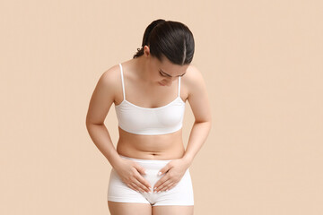Young woman in underwear suffering from cystitis on beige background