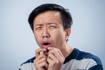 Asian man in striped shirt close-up showing a confused expression, raising eyebrows and touching...
